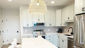 Une cuisine moderne avec des meubles blancs, un îlot central, des appareils en acier inoxydable et un luminaire suspendu en forme de lanterne.