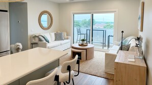 Un salon moderne avec un canapé blanc, un miroir rond, une table à manger et un balcon offrant une vue dégagée.