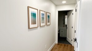 Un couloir aux murs blancs, doté d’un plancher en bois et orné de trois tableaux encadrés.