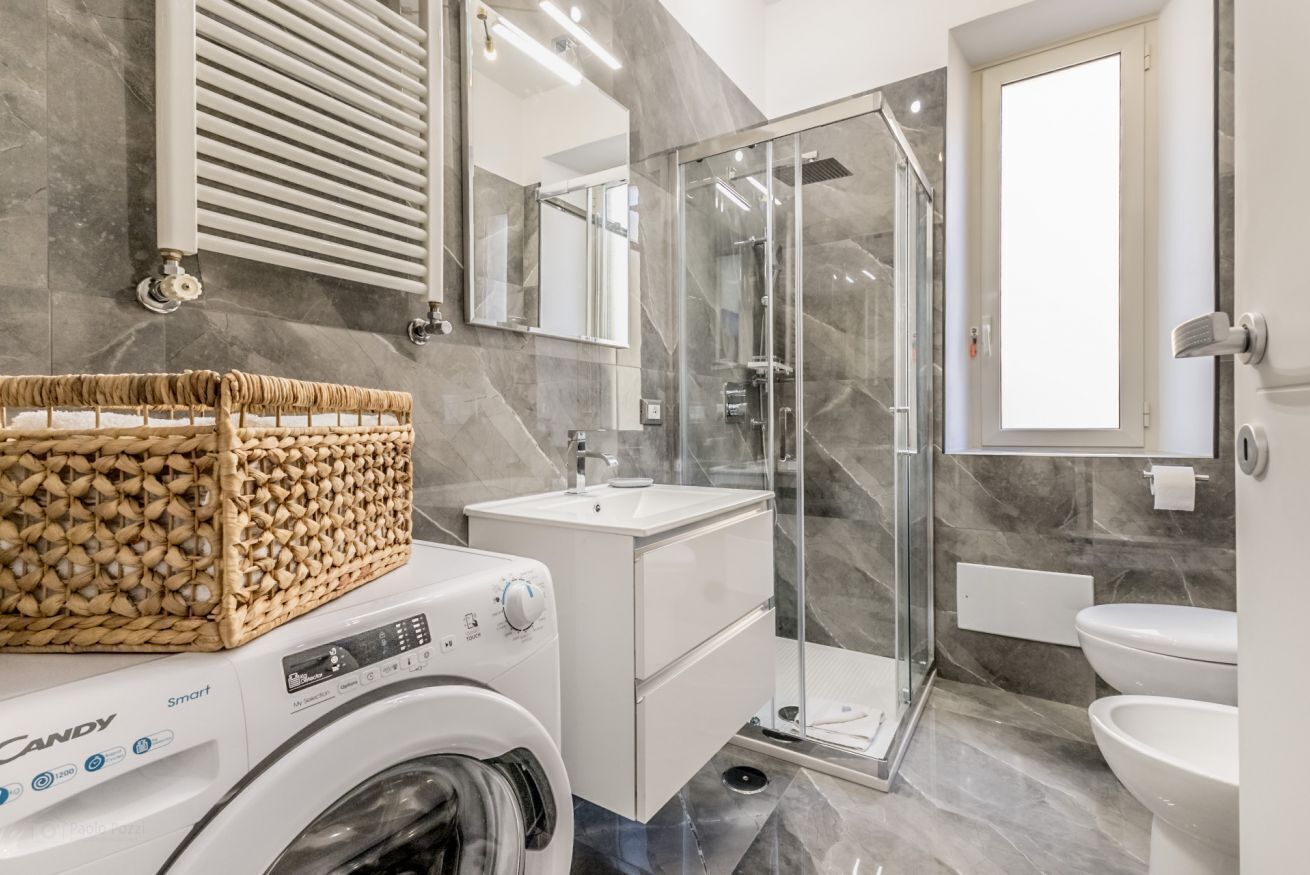 A modern bathroom with a glass shower enclosure, a built-in sink, and a washing machine.