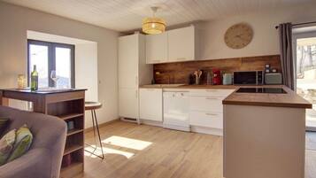 A modern kitchen with white cabinets, a wooden countertop, and a built-in dishwasher. There is a dining area with a table and chairs, and a large window providing natural light.