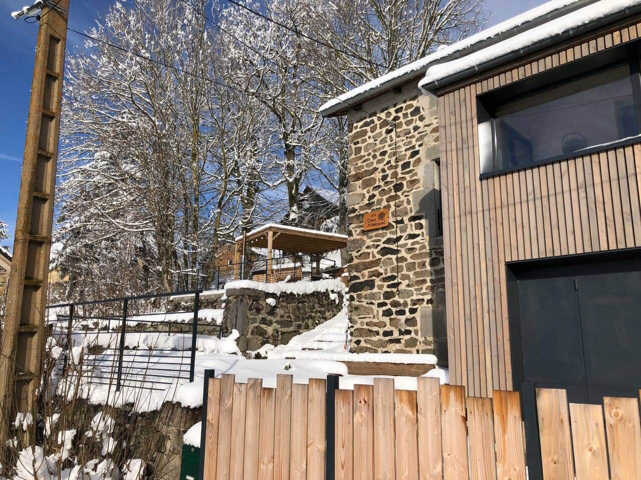 Un bâtiment en pierre doté d’une terrasse en bois et d’une clôture en métal.