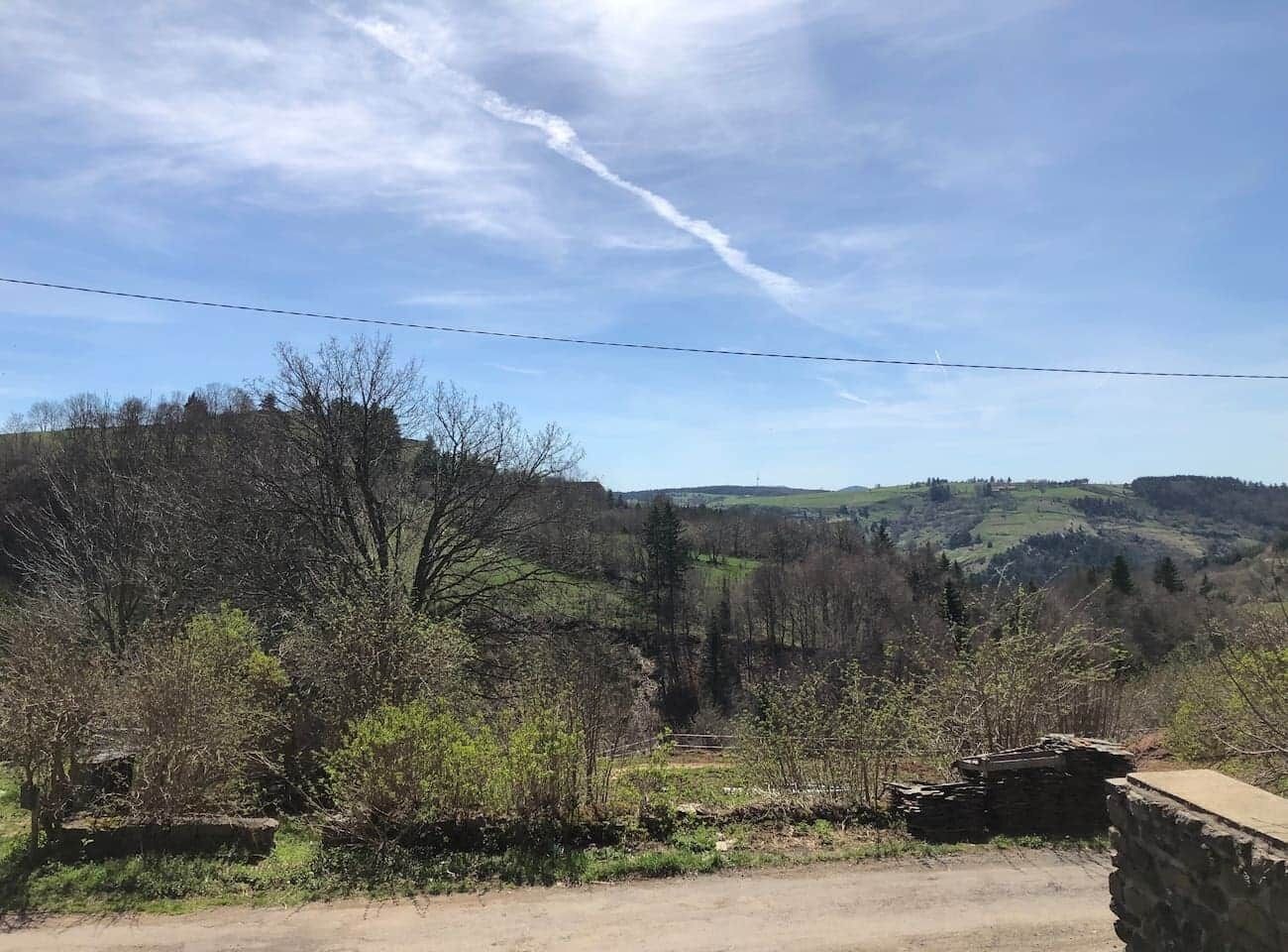 A rural landscape with a dirt road, stone structures, and trees.