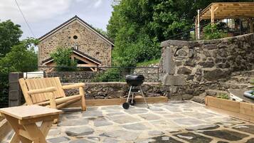 Een terras van natuursteen met een houten barbecue, een houten bank en een tafel.