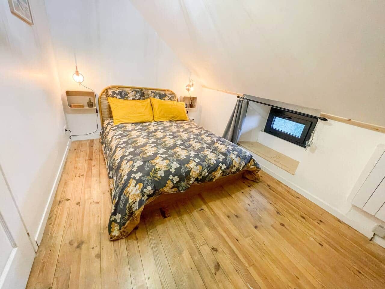 Camera da letto con pavimento in legno, un letto con biancheria a fiori, due comodini e una finestra con vista.