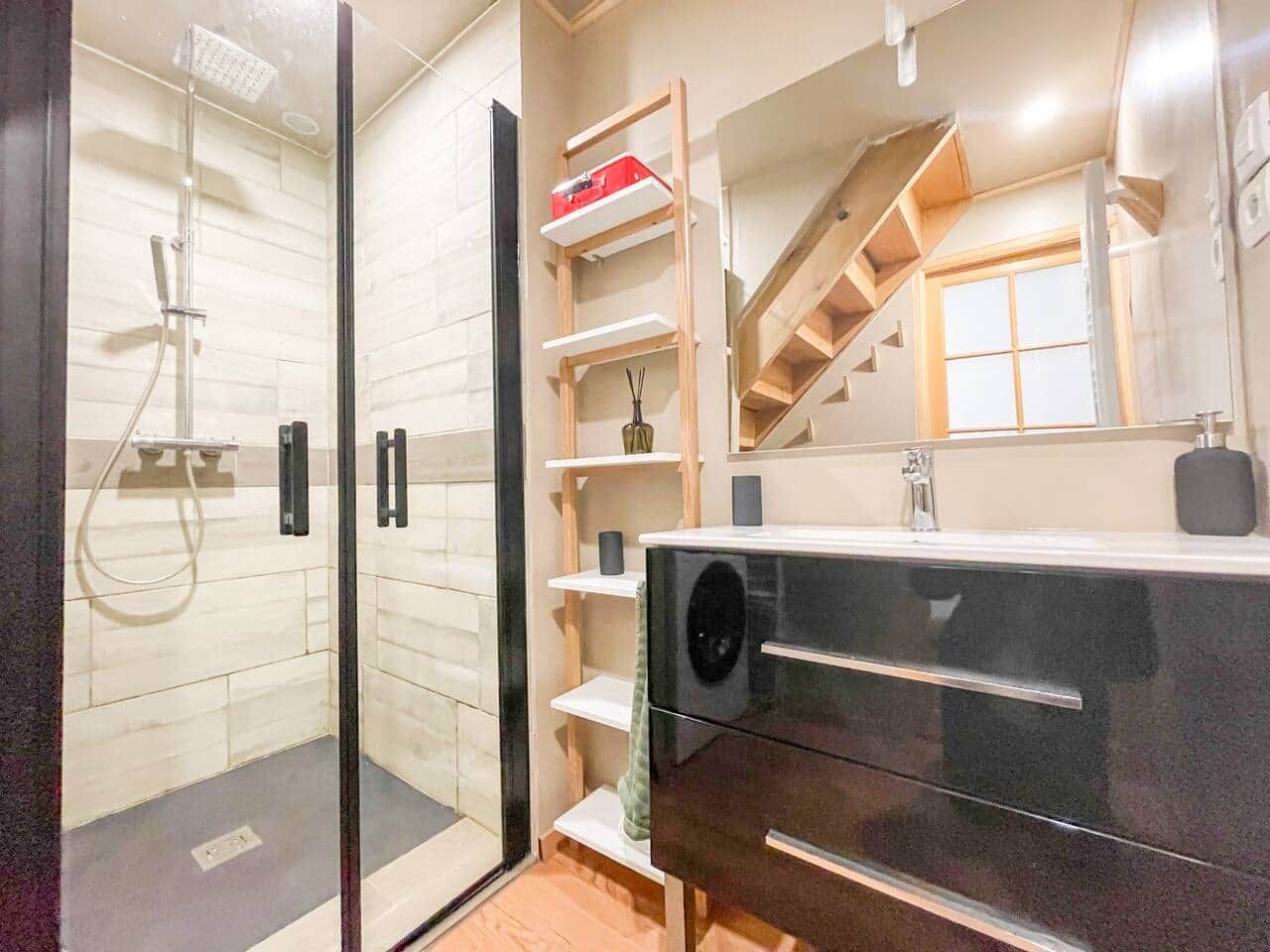 Une salle de bain moderne avec une douche à l’italienne en verre, un meuble-lavabo noir avec un miroir et un escalier en bois.