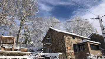 Une maison en pierre dotée d’un balcon en bois, entourée d’arbres couverts de neige.