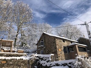 Una casa de piedra con balcón de madera, rodeada de árboles cubiertos de nieve.