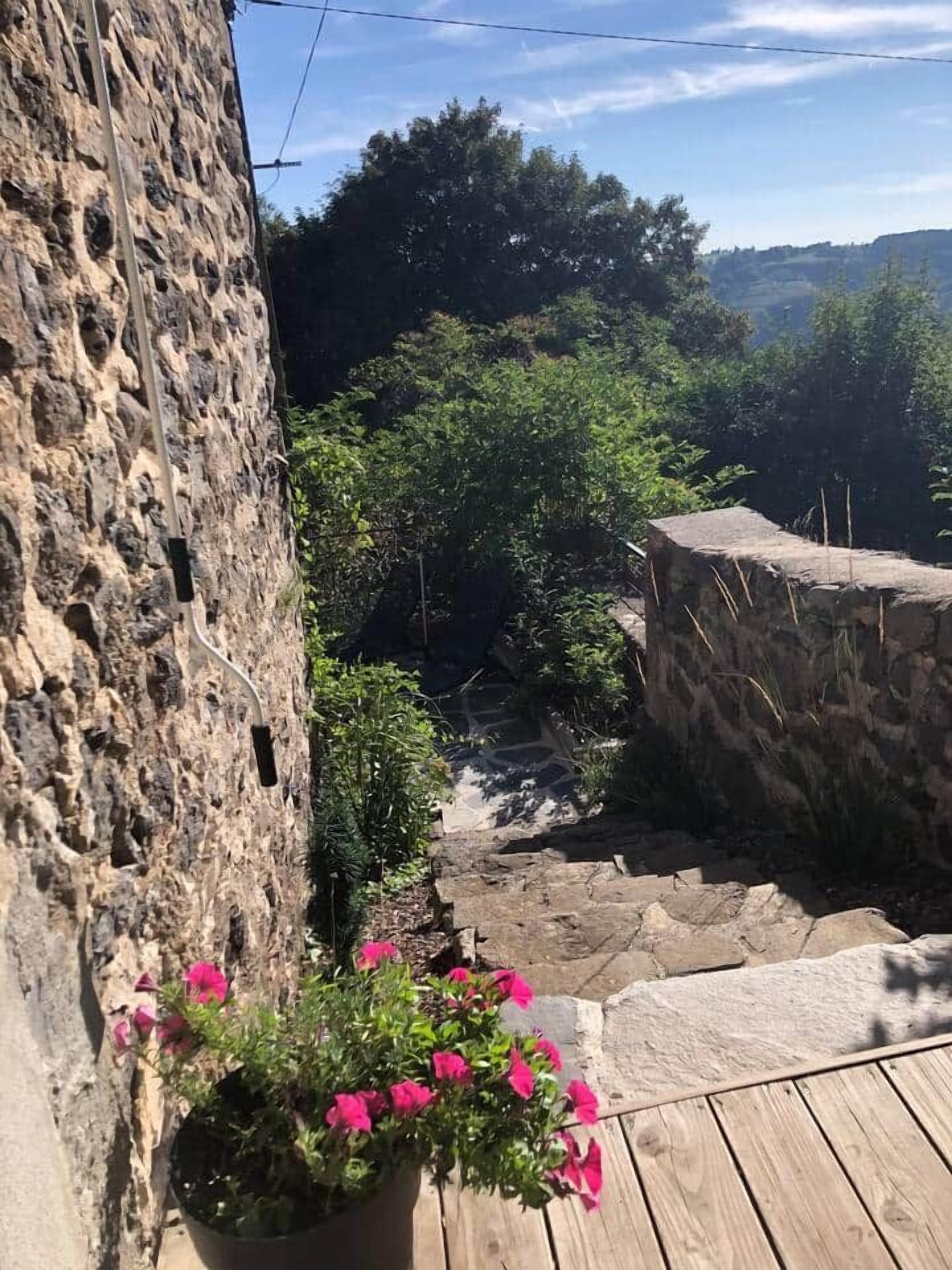 En stenmur, trästeg och en krukväxt med rosa blommor.