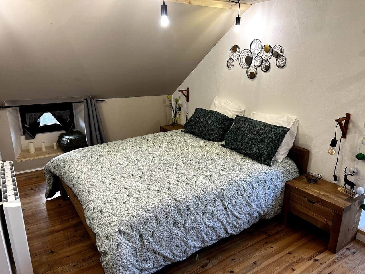 Un dormitorio con cama, piso de madera y ventana con cortinas.