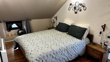 Un dormitorio con cama, piso de madera y ventana con cortinas.