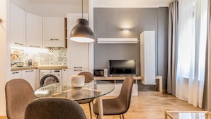A modern kitchen with a microwave, toaster, and washing machine. There is a dining area with a glass table and chairs. A TV is mounted on the wall, and a large pendant light hangs above the table. - Sapienza Apt - Modern House en Piazza Bologna (Rome)