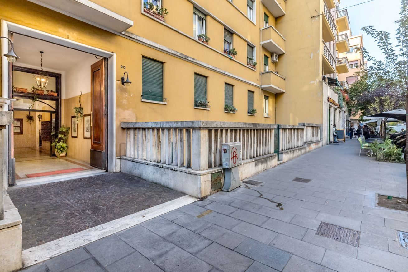 A yellow building with a wooden door, a metal railing, and a paved sidewalk.