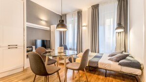 A modern, well-lit room with a bed, a dining table with chairs, a television, and a large window with curtains. - Sapienza Apt - Modern House en Piazza Bologna (Rome)