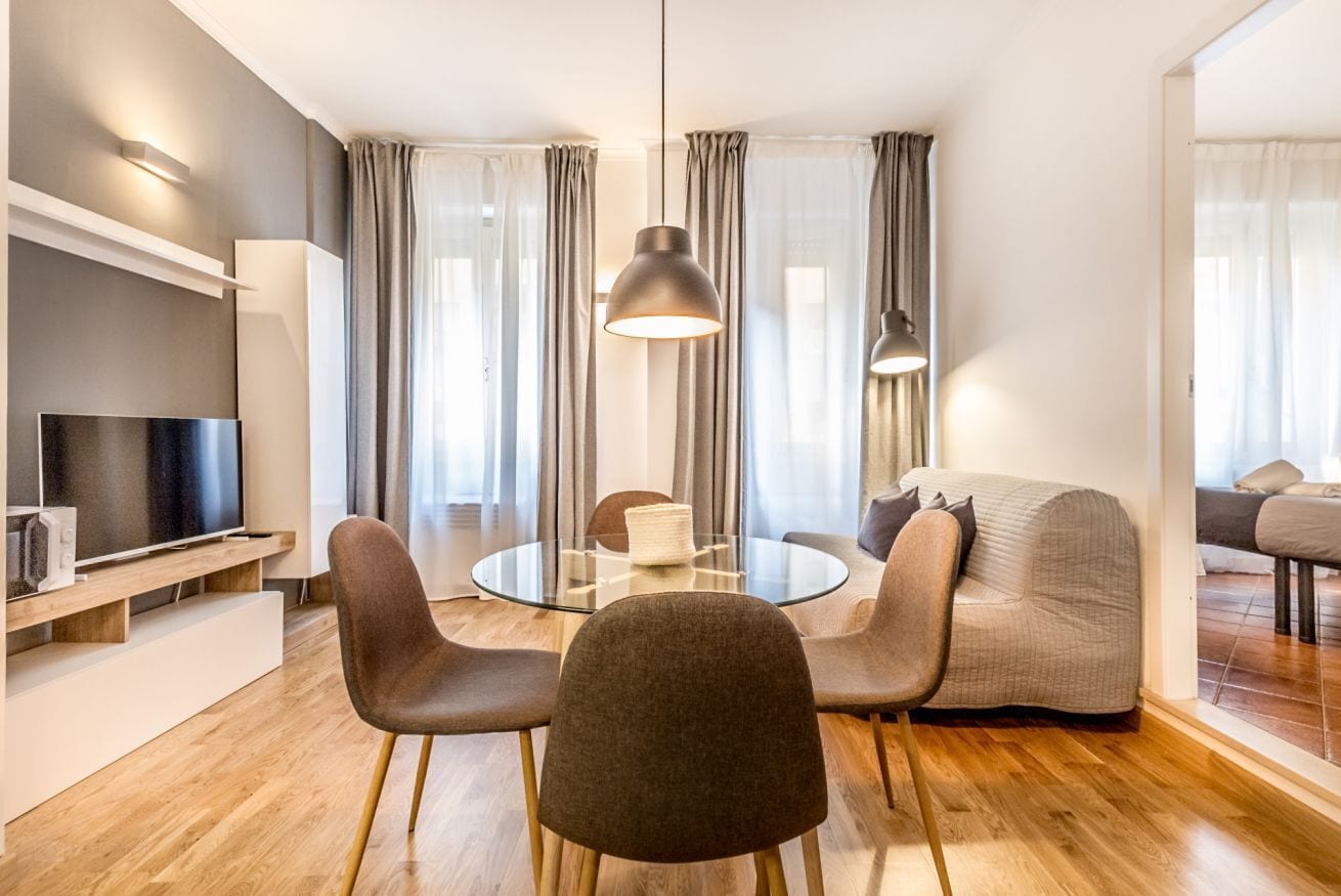 Ein modernes Wohnzimmer mit einem runden Glastisch, zwei Stühlen, einer Couch, einem Fernseher und einer Pendelleuchte.