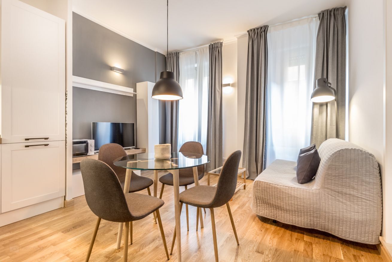 Ein modernes Wohnzimmer mit einem Glastisch, einem grauen Sofa und einem Fernseher im Hintergrund.