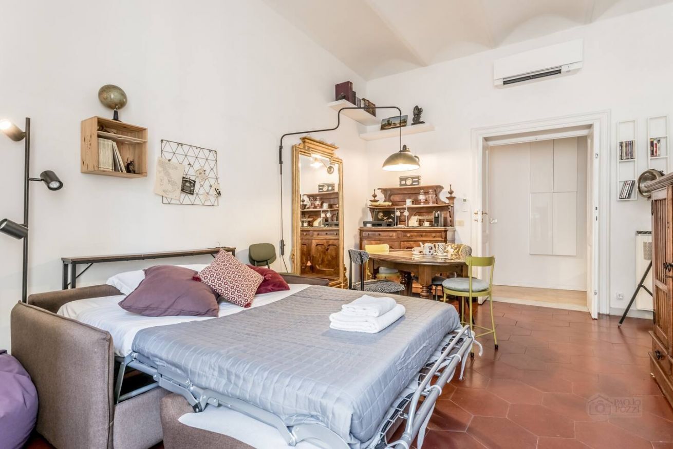 Een slaapkamer met een bed, nachtkastje en een stoel. Er is een houten kast en een spiegel aan de muur.
