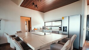 A modern kitchen with a large island, built-in appliances, and a dining area with a marble table and cushioned chairs. - Casa Dalia (Monteverde)