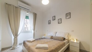 Ein Schlafzimmer mit einem Bett, einem Nachttisch, einem Fenster mit Vorhängen und Bildern an der Wand.