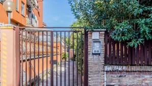 A gated entrance with a metal gate, a brick wall, and a number sign. - [Metro C] Nando's House (Roma)