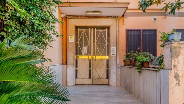 A building entrance with a metal gate, a wooden fence, and potted plants. - [Metro C] Nando's House (Roma)