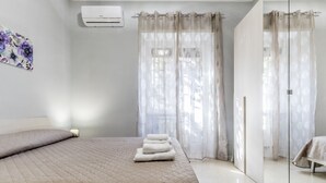 A bedroom with a bed, a bedside table, an air conditioner, and sheer curtains. - [Metro C] Nando's House (Roma)