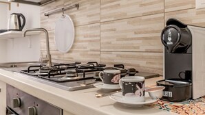 A modern kitchen with a gas stove, coffee maker, and a hanging pot rack. - [Metro C] Nando's House (Roma)