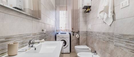 A modern bathroom with a large sink, a washing machine, a bidet, and a toilet.