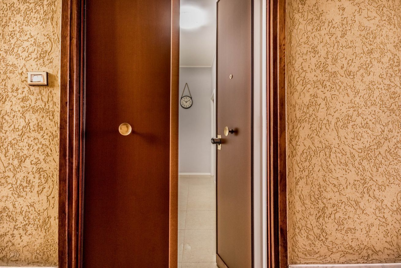A wooden door with a round handle and a keyhole, leading to a bathroom with a tiled floor and a wall-mounted clock.
