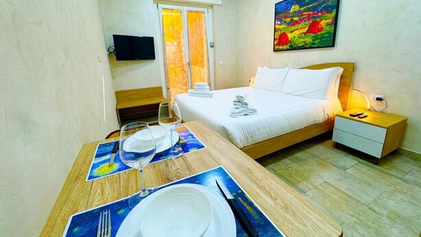 A hotel room with a bed, bedside table, and a dining area with a table set for two. - La Palmetta (Near Metro A) (Roma)
