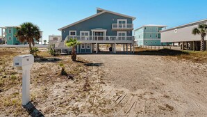 A beachfront house with a covered porch, a mailbox, and a sandy driveway.