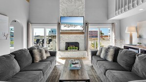 A modern living room with a fireplace, two grey sofas, a coffee table, and a TV mounted on a stone wall.