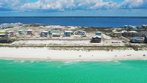 An aerial view of a coastal hotel with multiple buildings, a sandy beach, and a clear blue ocean.