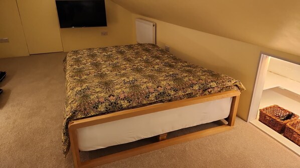 A bedroom with a bed, a television mounted on the wall, and a radiator.