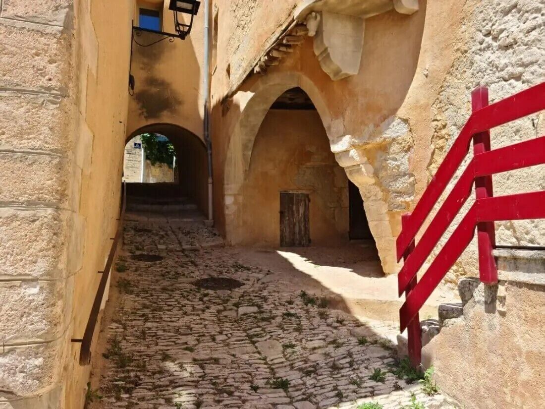 Une ruelle étroite pavée de pierres, avec une porte rouge et des murs en pierre.