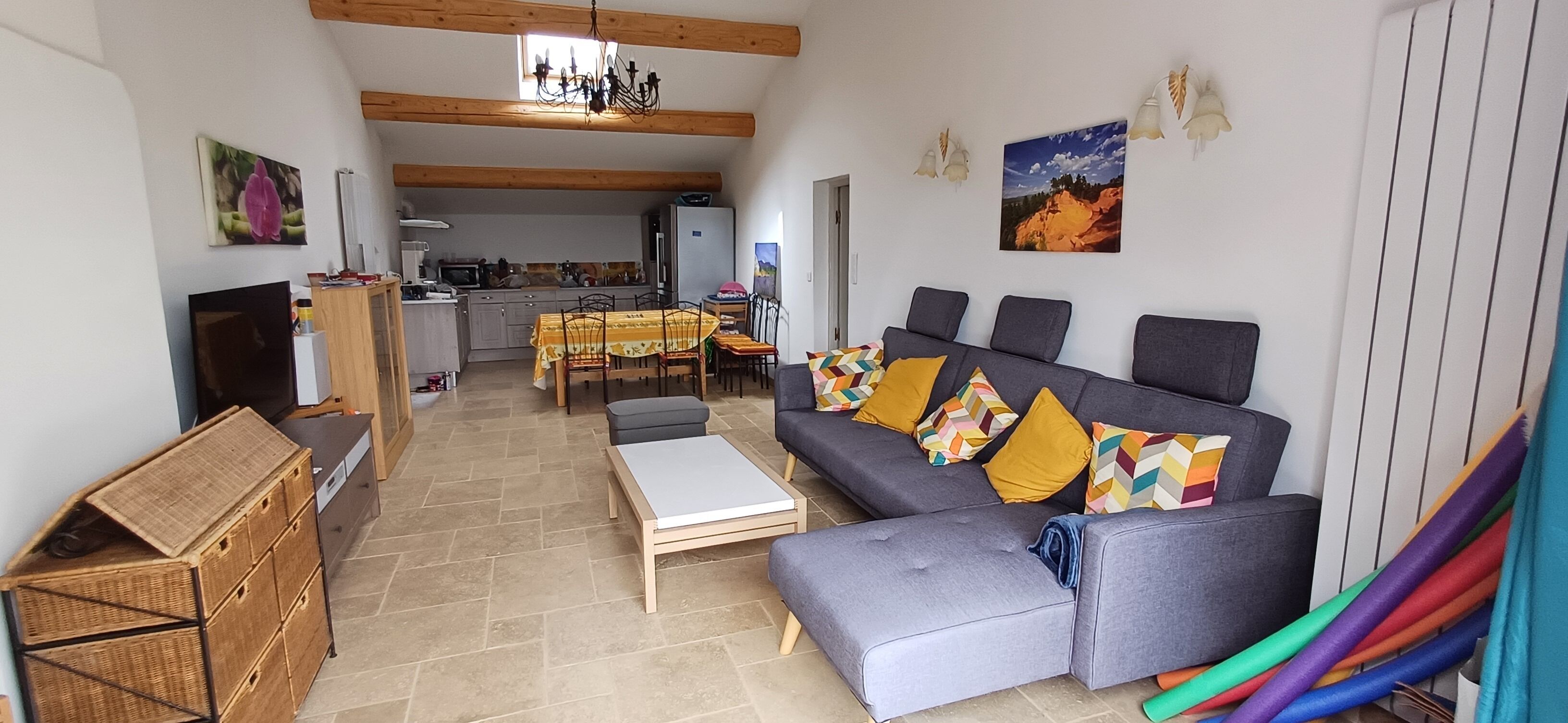 Un salon chaleureux avec un canapé gris, une table basse en bois et un coin repas comprenant une table et des chaises.