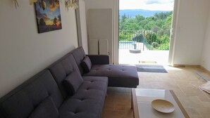 A modern living room with a sectional sofa, a wooden side table, and a view of a balcony with a pool. - Quiet - Charming - Atypical - View Luberon - Parc Naturel du Luberon - GR97 (Saint-Saturnin-Lès-Apt)