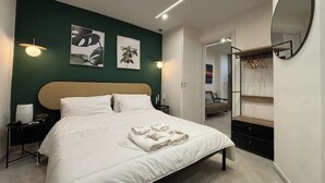Une chambre d’hôtel moderne avec un grand lit, une table de chevet, une armoire et un miroir au mur.