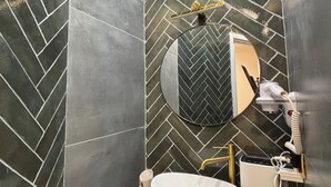 Une salle de bain avec un carrelage disposé en motif chevron, un miroir rond, un lavabo blanc et un sèche-cheveux.