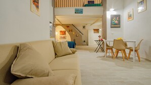 A living room with a beige sofa, a dining table with chairs, and a staircase leading to an upper level. - MIMI HOUSE IN THE HISTORIC CENTRE (Naples)