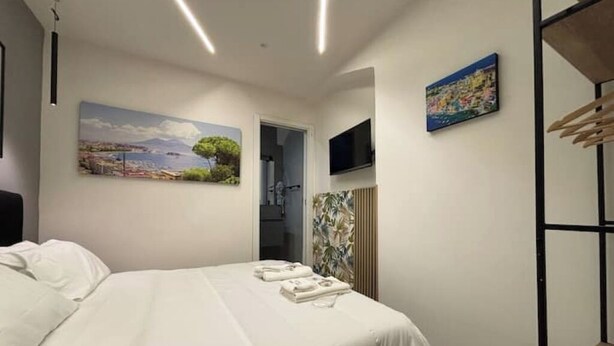 A bedroom with a bed, a painting, a television, and a wardrobe. - House in the heart of the historic center of Naples - Small Apartment (Napoli)