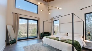 A spacious bedroom with a four-poster bed, large windows, and a view of the outdoors. - Luxury Lake Lure Vacation Rental | Sleeps 12+ | Rumbling Bald Resort | Hot Tub (Lake Lure)