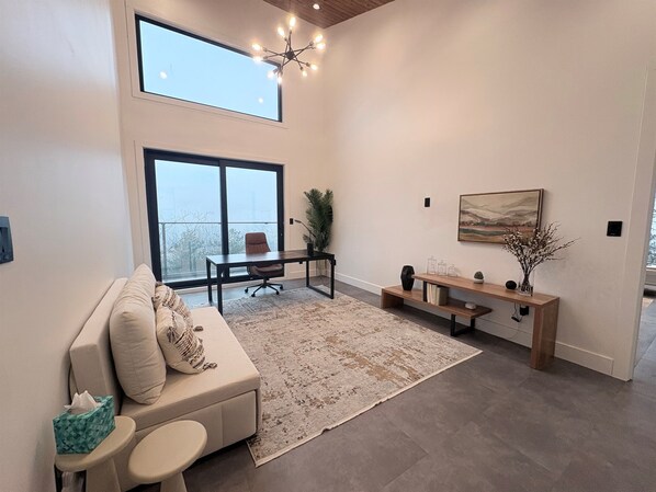 A modern living room with a sofa, a coffee table, a desk, and a large window.