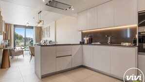 A modern kitchen with a central island, built-in appliances, and a dining area with a view. - Calanova Escape | terrace - pool - golf (La Cala de Mijas)