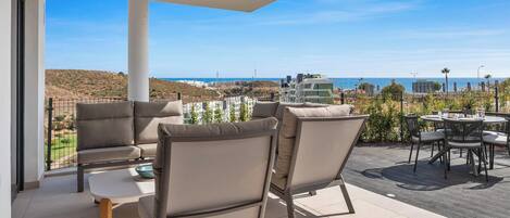 Une terrasse avec des sièges extérieurs, une vue dégagée sur la mer et un bâtiment moderne en arrière-plan.