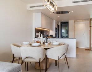 A modern dining area with a round table, four chairs, and a kitchen in the background.