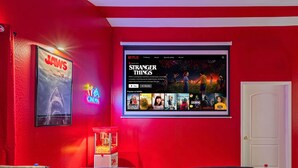 A home theater room with red walls, a large screen displaying a Netflix series, popcorn, and black leather chairs. - Sleeps 20! Movie Theater, Arcade & King Suites near Stadium (Glendale)