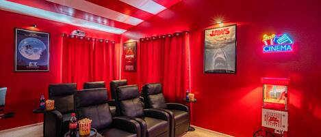 Une salle de cinéma à la décoration rouge, avec des fauteuils inclinables en cuir noir, des seaux à pop-corn et un appareil à pop-corn d’époque.