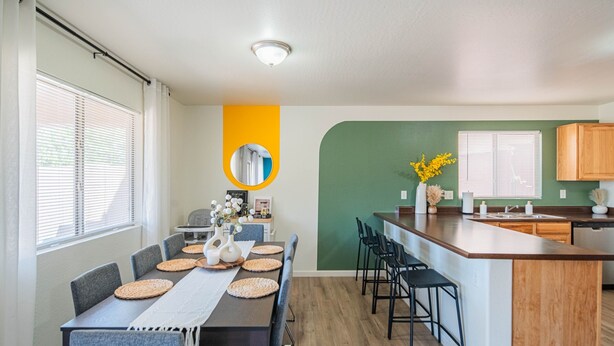 A modern kitchen with a wooden island, a dining area with a long table and chairs, and a green accent wall. - Sleeps 20! Movie Theater, Arcade & King Suites near Stadium (Glendale)