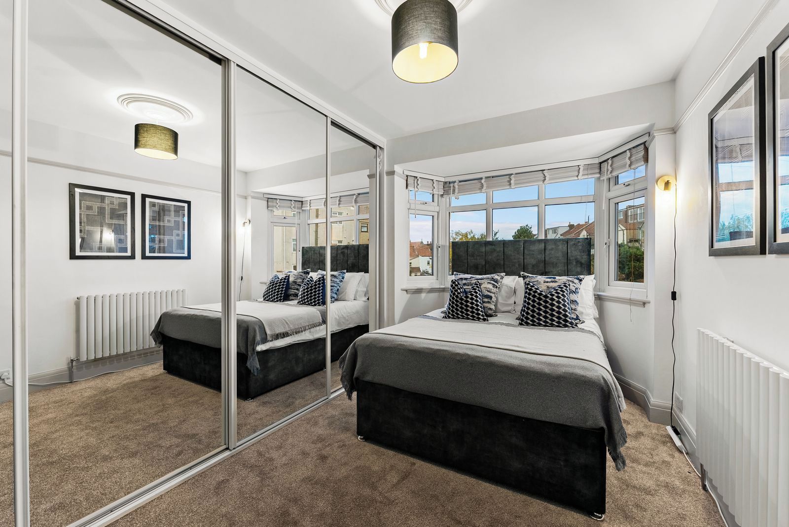 A bedroom with a large mirror, two beds, a radiator, and a view of the outside.